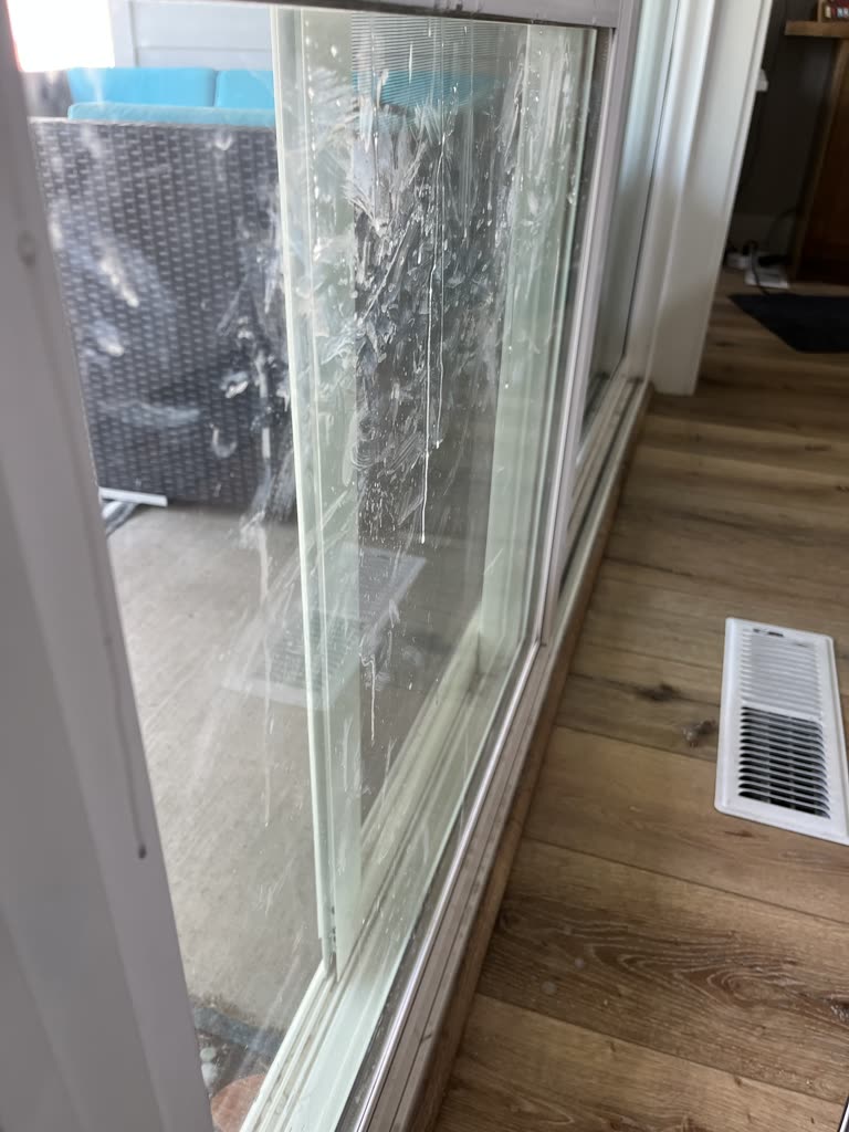 A sliding glass door before cleaning, the inside of the glass streaked with dried hard water