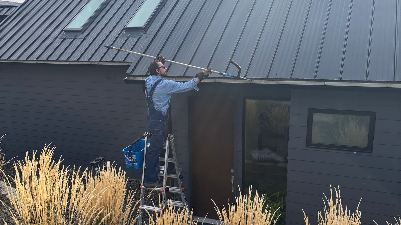 A Seymour's tech on a ladder at the roofline of a dark modern home
